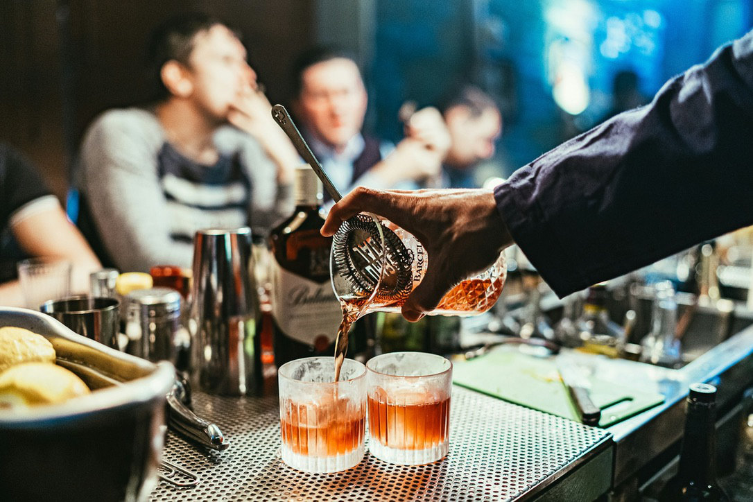 Bartender pouring cocktail into glass at a bar